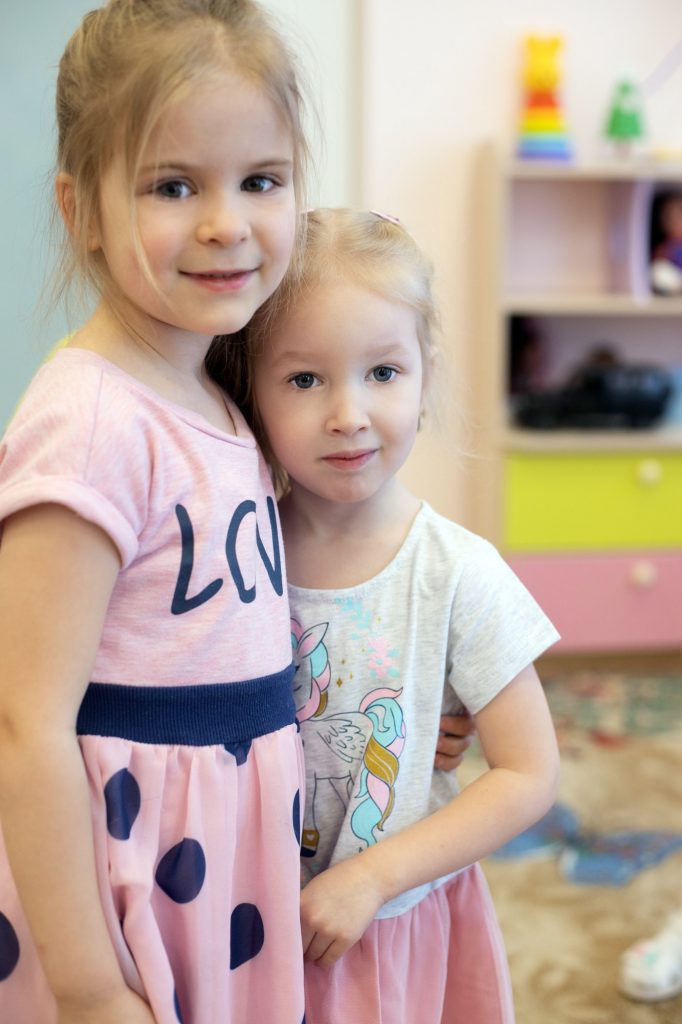 Two kid girls in kindergarten. Looking at camera. Friends or sisters. Happy childhood. Vertical